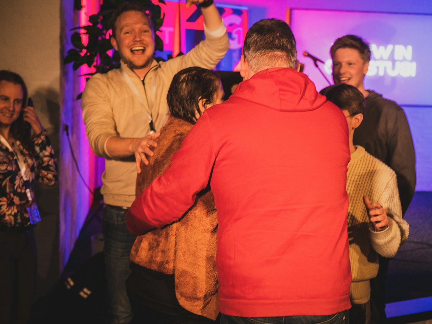 Persone diverse festeggiano a un evento al chiuso con luci colorate.