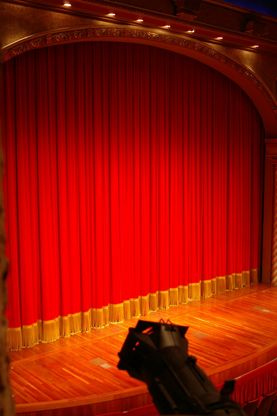 Palco di un teatro vuoto con tende rosse e finiture dorate.